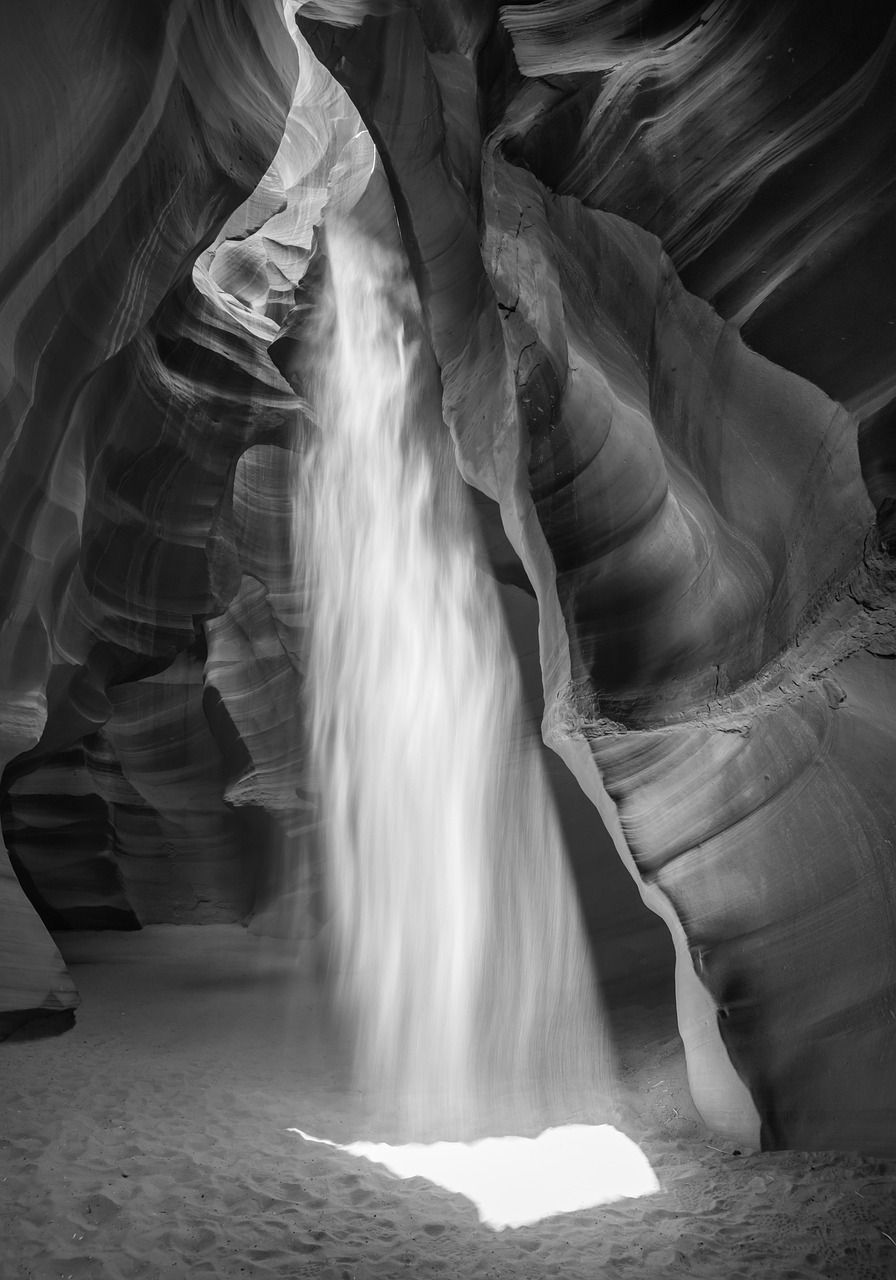 Black and white photo of Antelope Canyon, highlighting smooth, swirling rock formations with light streaming through a narrow opening above.