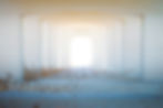 Symmetrical view of a white concrete corridor with dry grass at the bottom. The bright light at the end creates an ethereal mood.