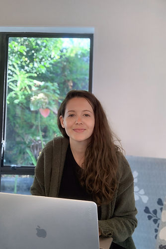 Jennifer Johnson, NZ Copywriter, wearing green jumper and black shirt sitting in front of laptop with window in background
