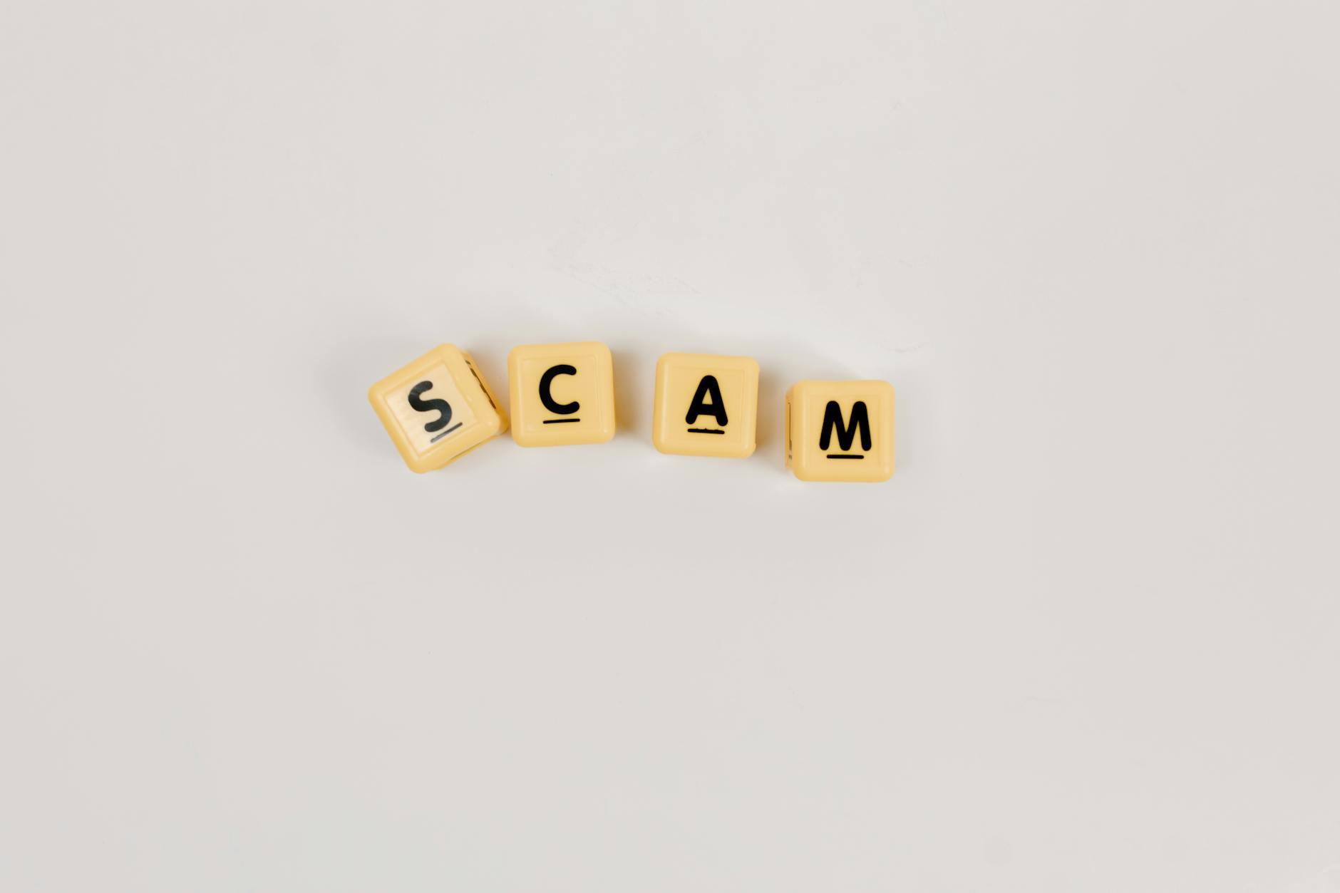close up shot of letter blocks that read "scam" on a white background