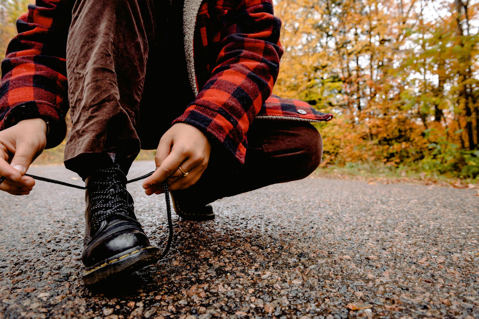 Person wearing red shirt to bend down to tie laces on boots outdoors