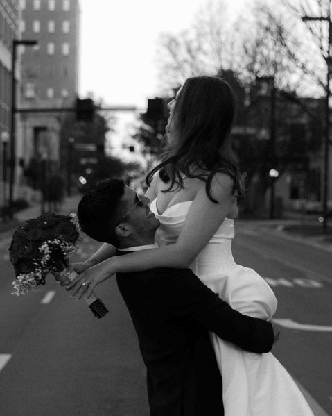 Groom lifting bride in the middle of a city street at sunset, romantic black and white wedding photo