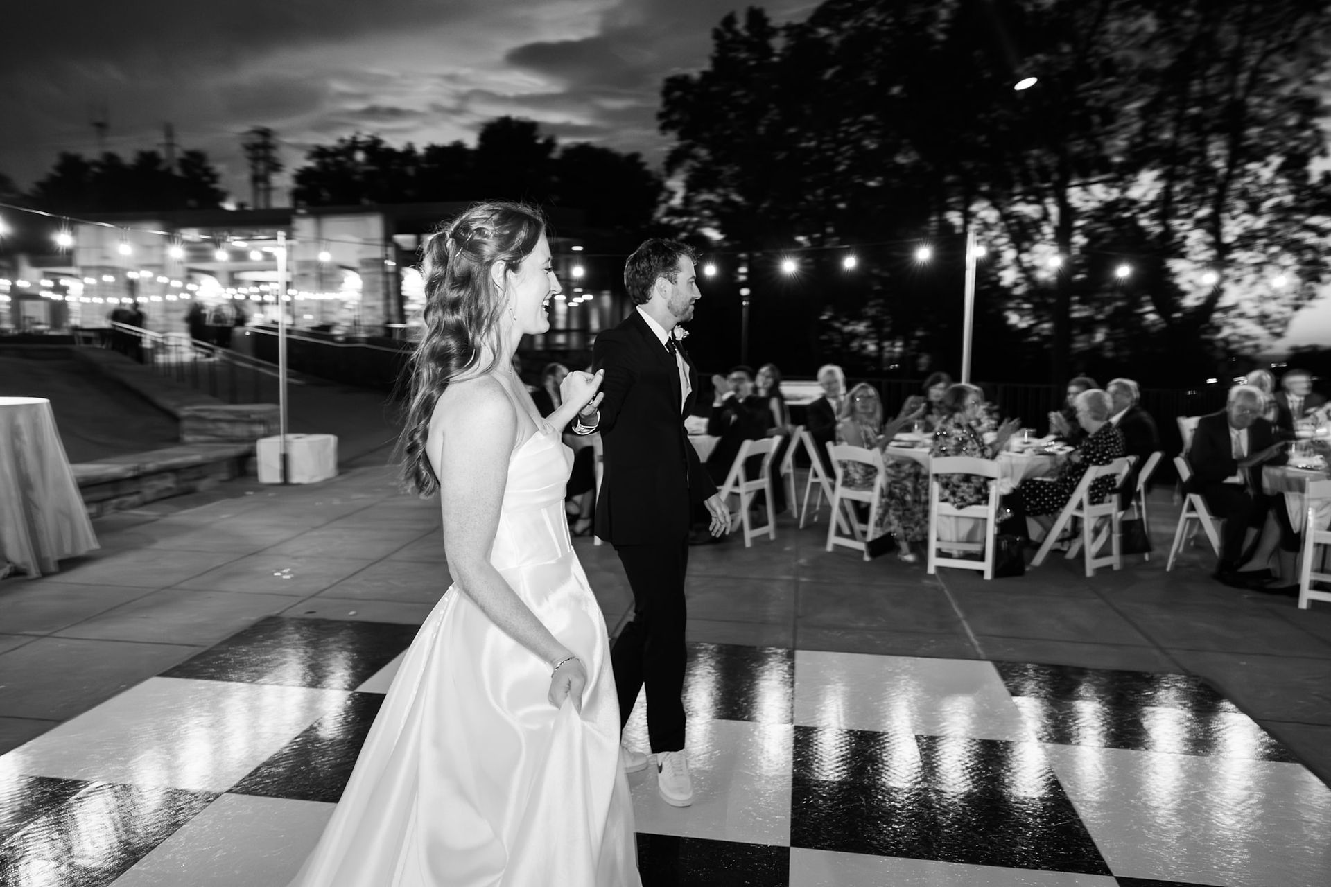 Candid black and white image of newlyweds walking onto the dance floor for their first dance