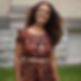Portrait photo of Jacki Trelawny wearing rusty patterned dress, blurred background of building exterior and grass