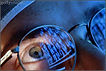 Close up image of a doctor showing his left eye looking through his gold rimmed glasses at multiple MRI images that are reflected in the glasses in cold blue light. Only his eye is seen with correct color.