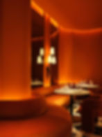 Orange lounge with curved seats, white marble tables set with glasses. Warm lighting creates an inviting, elegant atmosphere. No text visible. GRAY Awards. GRAY magazine. Hospitality design.