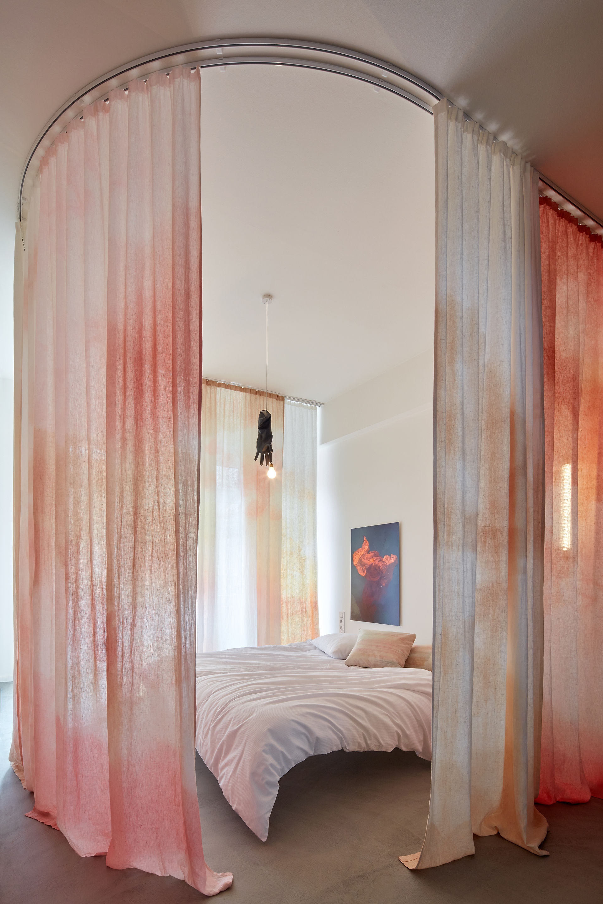 bedroom with sheer curtains in orange and pink acid wash on ceiling track, black Luzy Ingo Maurer pendant light, white bed linens