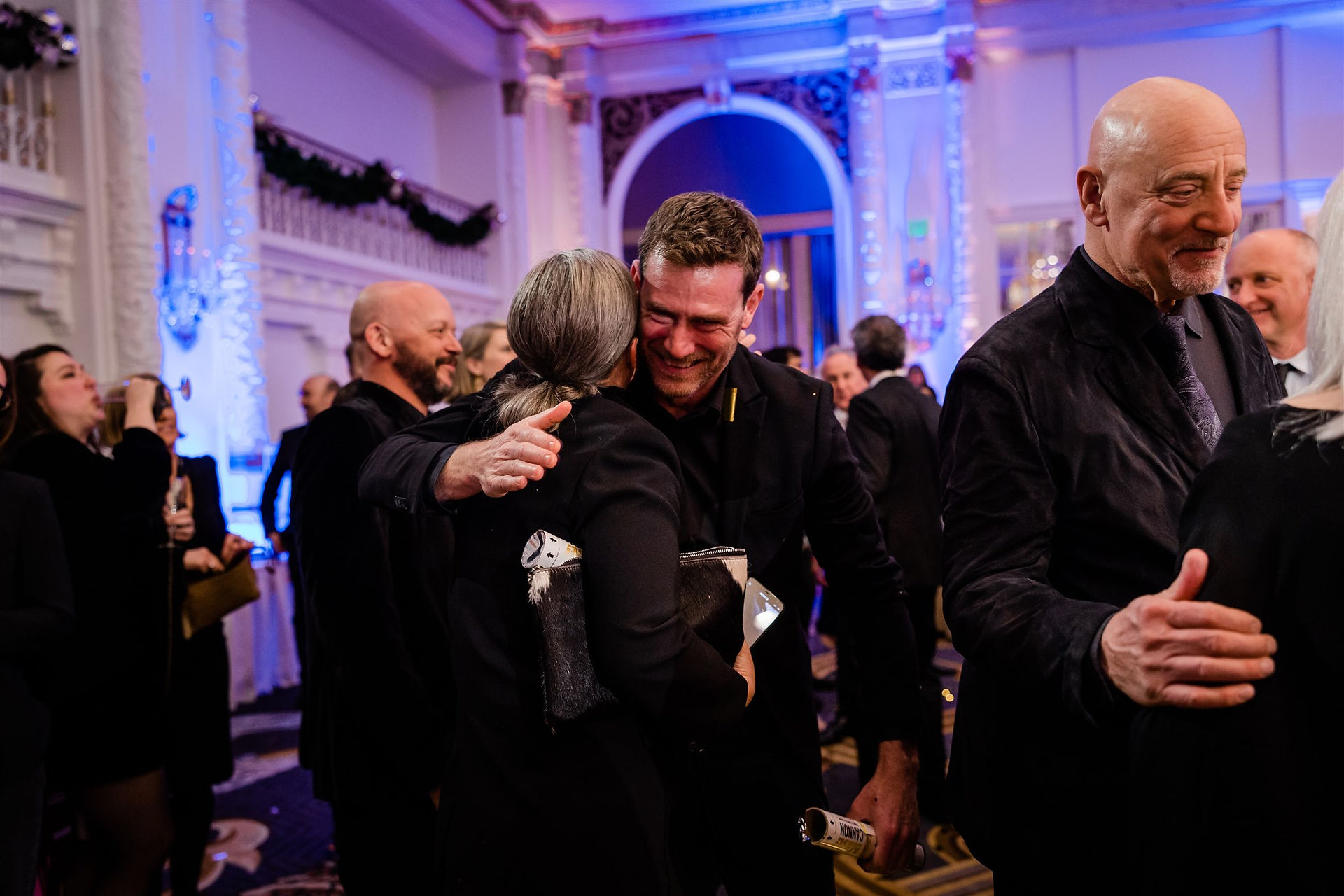 Party guests celebrating and hugging in ballroom at formal gala