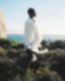 Woman standing on shore looking out at ocean, designer clothing, white apparel, South African fashion designer Rich Mnisi’s Spring/Summer 21 collection, Hiya Kaya