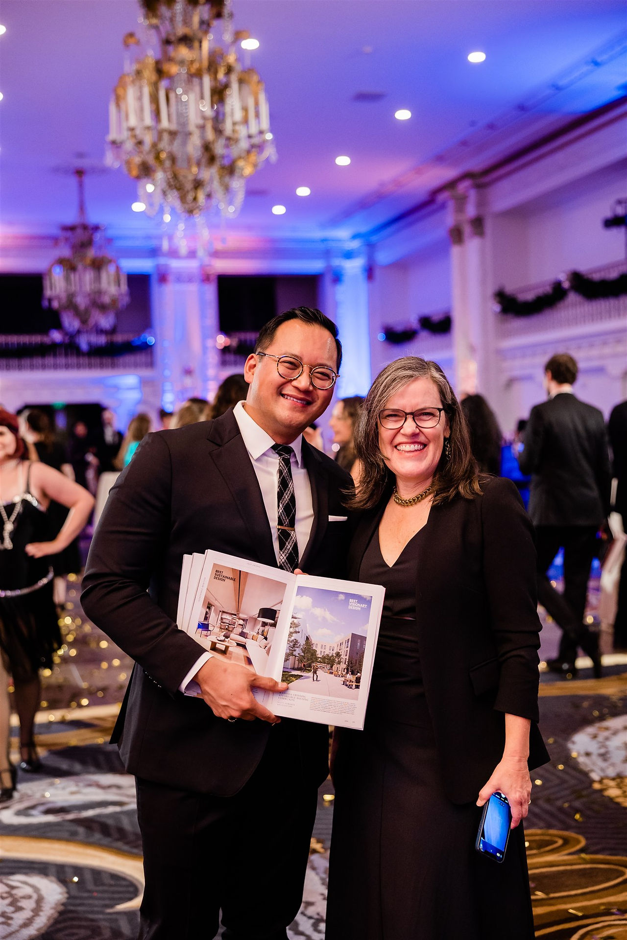Party guests holding open design magazine in ballroom at formal gala