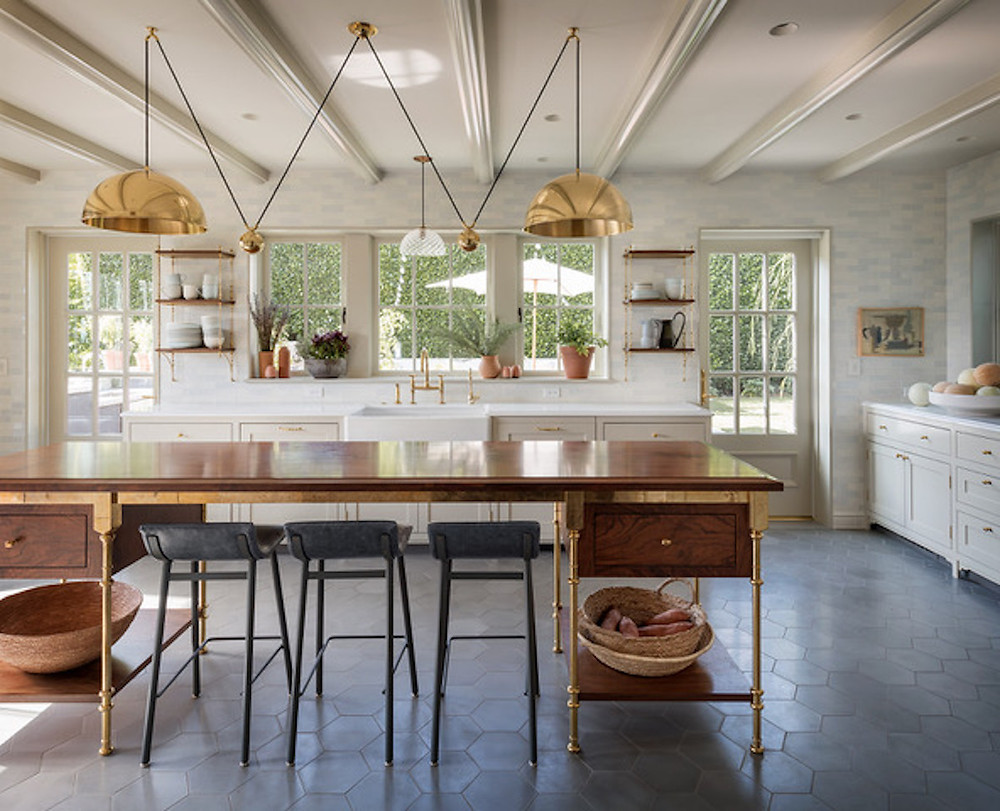 farmhouse kitchen with tile floor, gold pendants, gold accents, farm table island, black bar stools, apron sink, open shelving