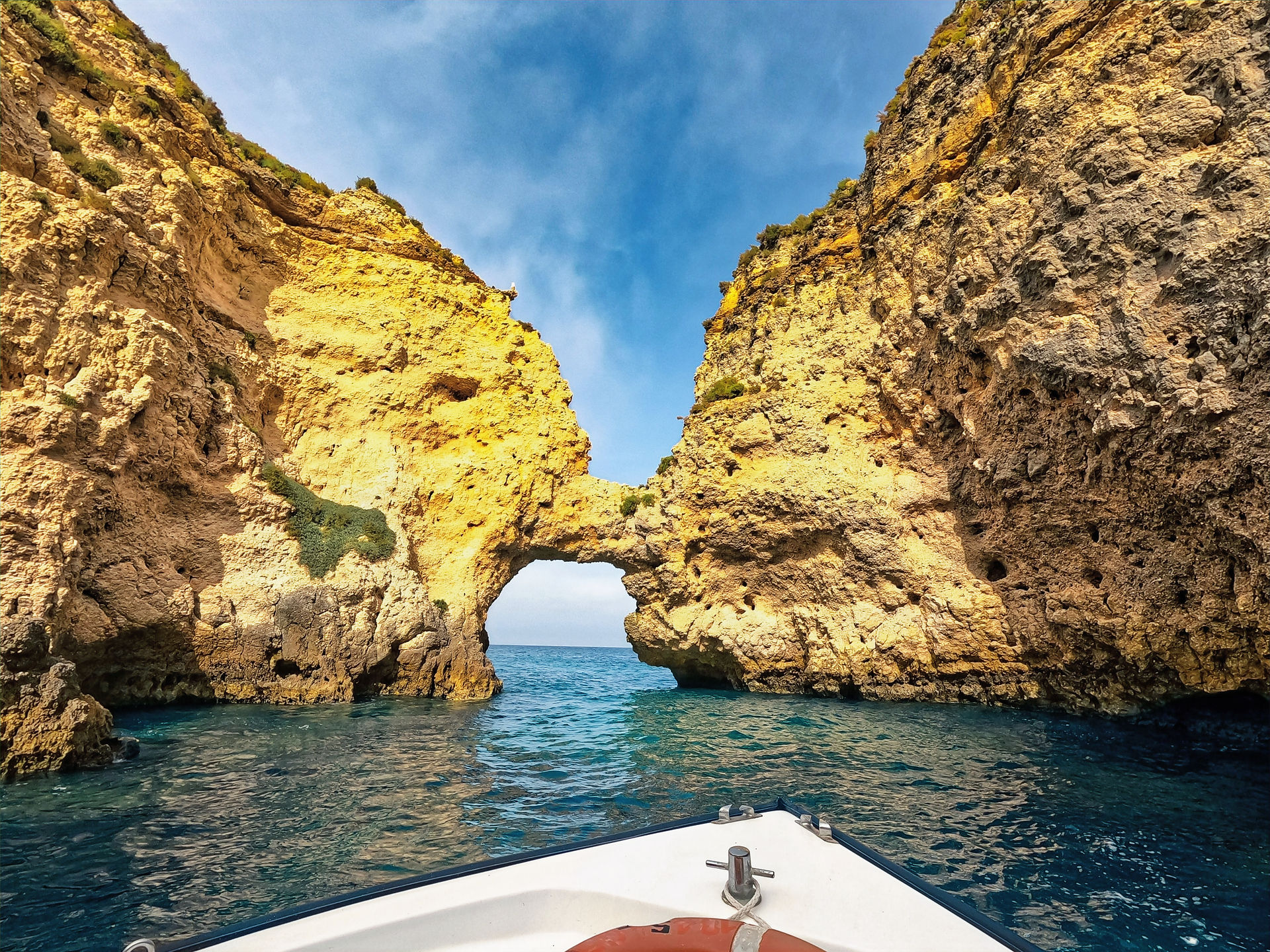 Die Spitze eines Bootes ist in der unteren Hälfte des Bildes zu sehen. Dahinter befindet sich das Meer und ein Bogen aus Gestein durchläuft das gesamte Bild. 