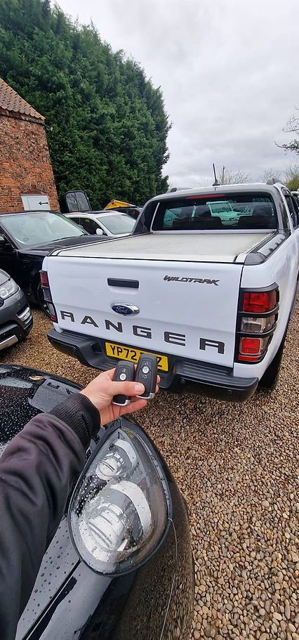 Hand holding two Ford key fobs in front of white Ranger Wildtrak pickup truck