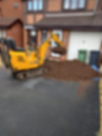 Yellow mini excavator moving a large pile of topsoil on a driveway
