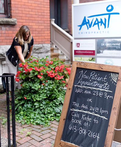 Woman tending red flowers outside Avanti, chalkboard with phone number