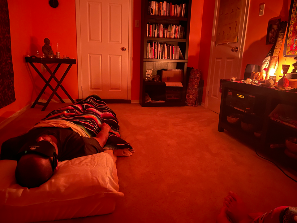 Man lying down, wearing eye mask near shelves of books, orange room setting.