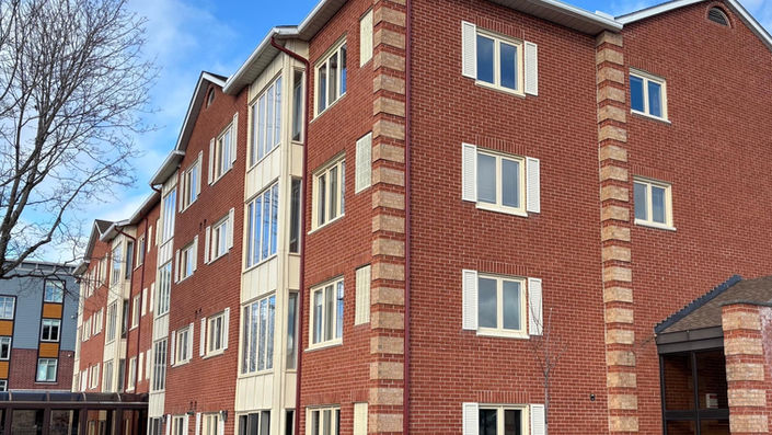 Multi-story residential building with red brick, white shutters, and green lawn.