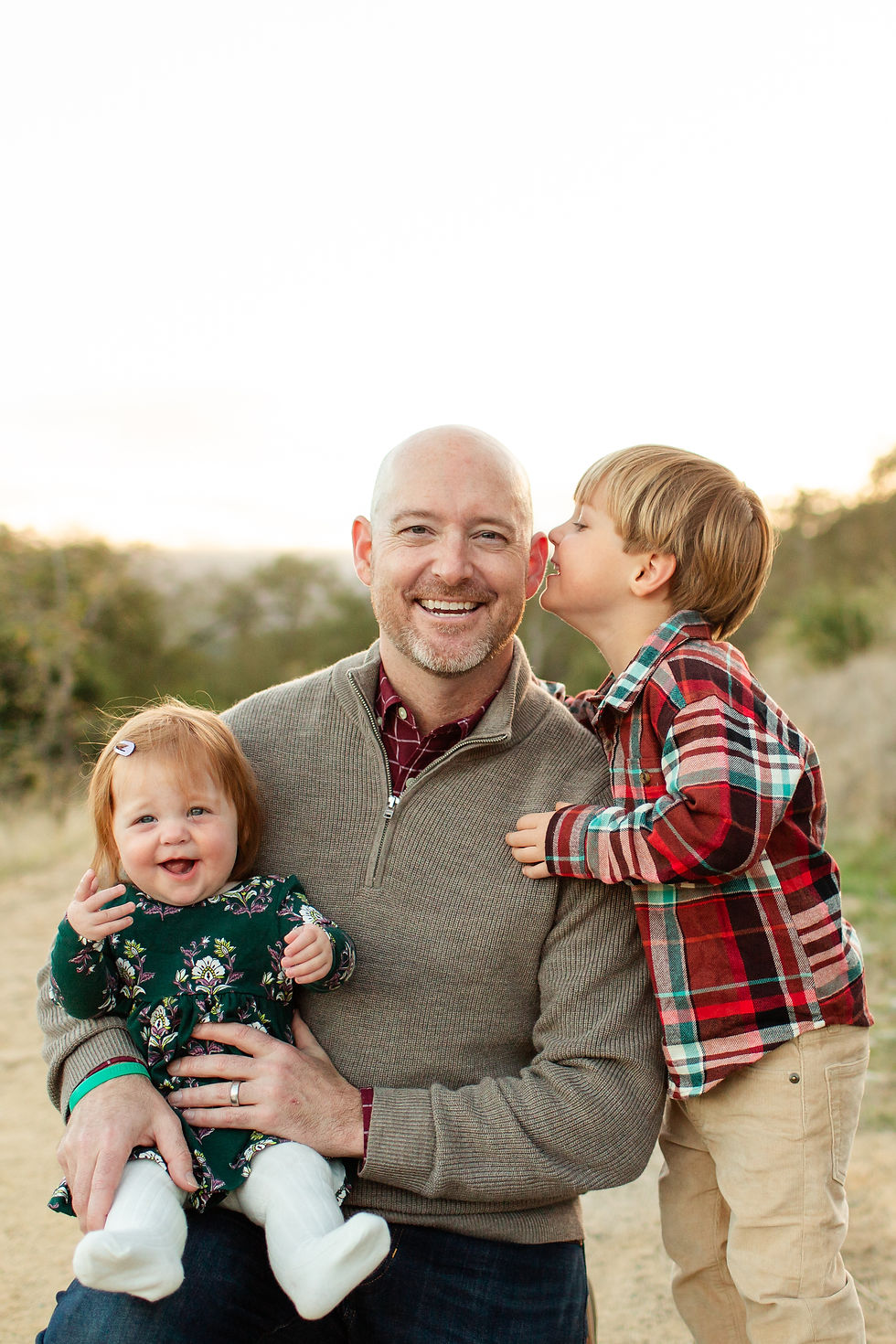 Father with two children outdoors; son whispers to him while daughter smiles. Boy in plaid, girl in floral dress. Warm, joyful setting.
Guadalupe Oak Grove Park in San Jose Winter Family of Four Photo Session during sunset by HKCreate Bay Area Photographers