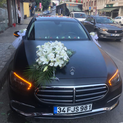 Siyah Mercedes çiçeklerle süslenmiş, 34FJS941 plaka, dış çekim, sokak görüntüsü.
