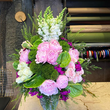 Pembe ve beyaz çiçek buketi, yeşil yapraklar ve vazoda duruyor.