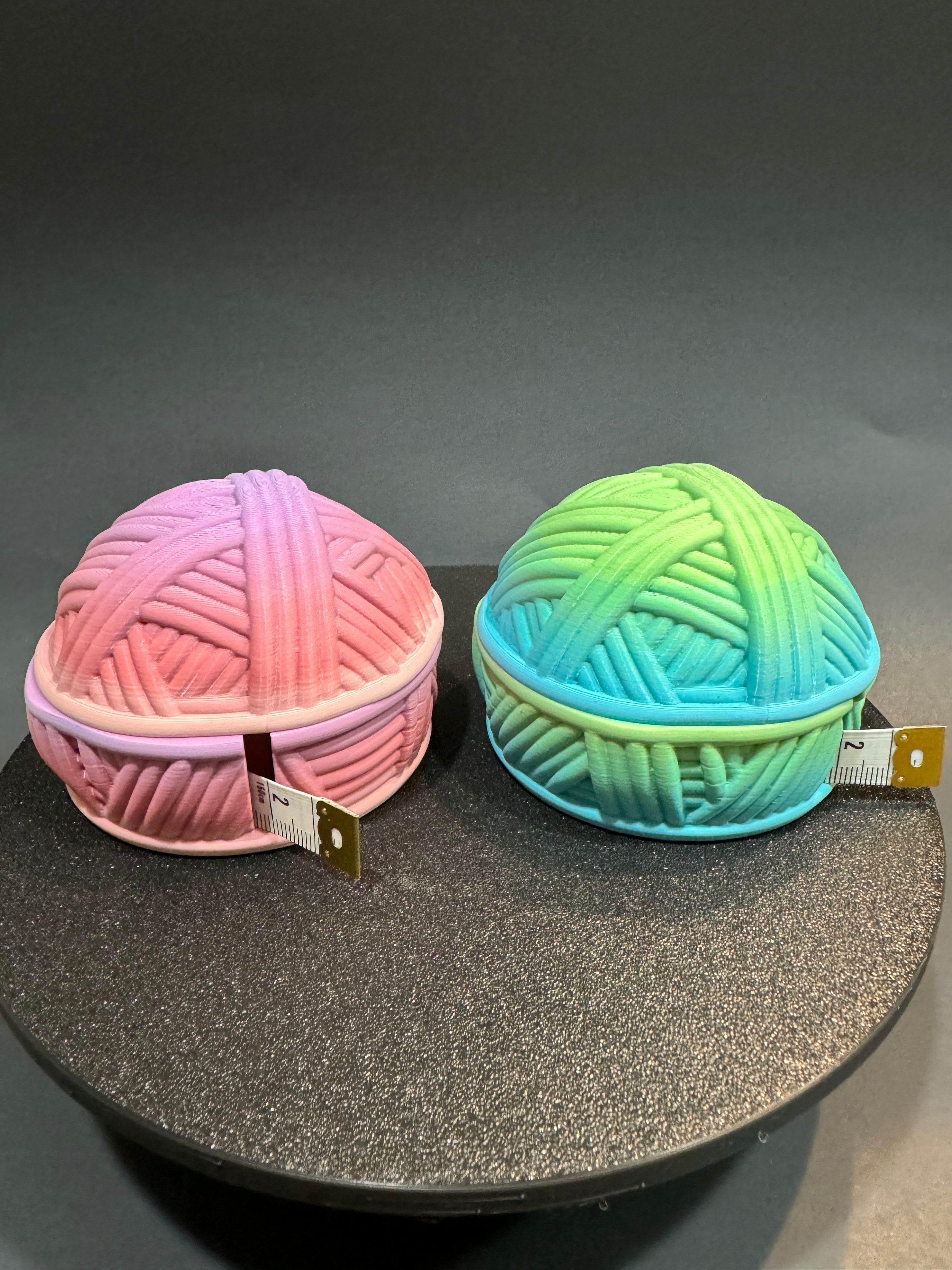 Two yarn ball tape measures in pink and green, with tape extended.