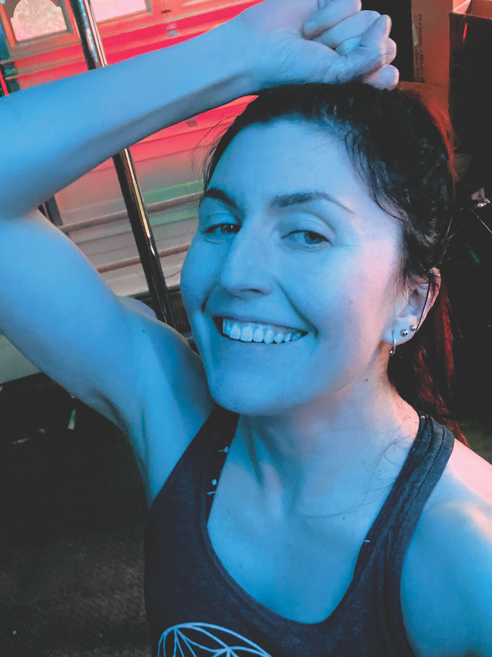 Smiling woman poses with arm raised in blue lighting. Red and green stripes in the background. She wears a tank top with a geometric pattern.