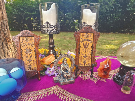 Blue eggs in a glass bowl on a purple altar cloth, with flowers, a bronze deity statue, and a carved sign reading EITHRA.