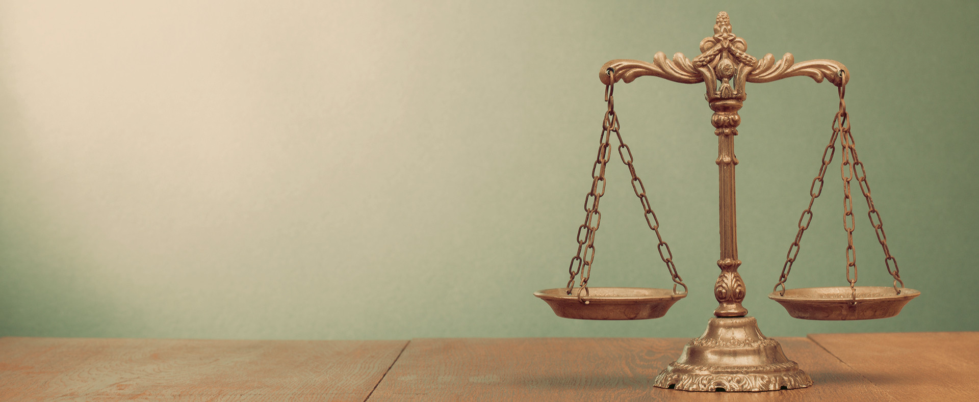 Brass balance scale on a wooden table against a green background, symbolizing justice and fairness.