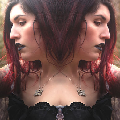 A woman with long red hair and black lipstick is mirrored, creating a symmetrical effect. She's wearing a pendant necklace and a black top.