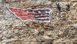Ancient rock art on stone depicts a red, wing-like shape and a figure with antlers. Earthy tones create a mysterious, historical feel.