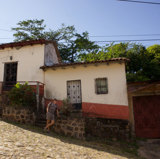 a man lounged against traditional small colonial style home painted in earthen colours