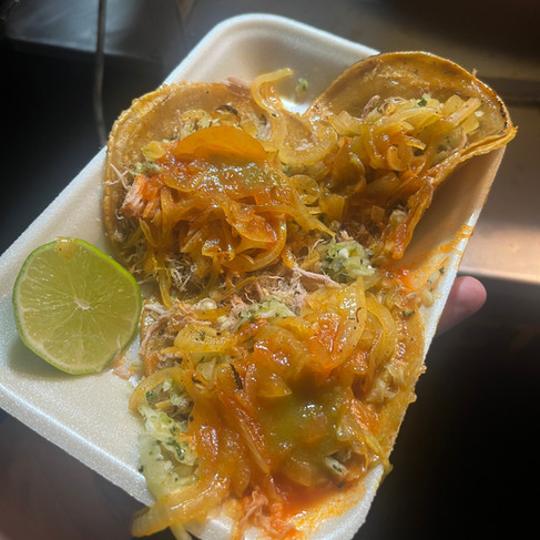 styrofoam plate holds three xela style tacos, with wet tortillas filled with pork, cooked onions and herby slaw