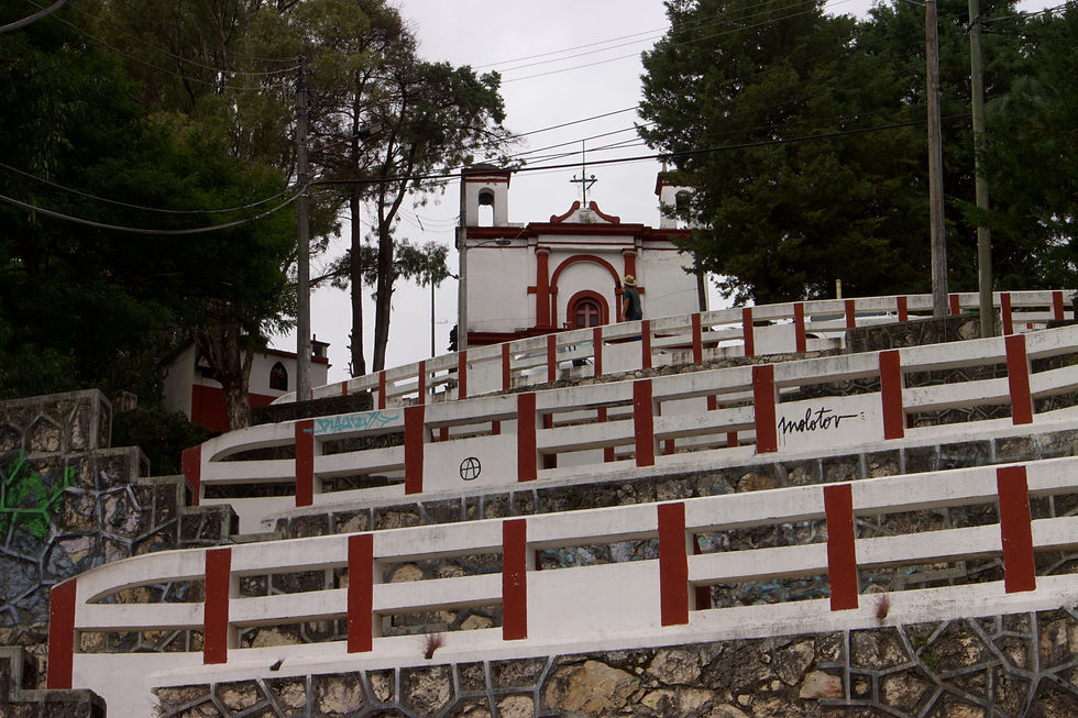 White and red stairway with graffiti leads up to a church with trees and overcast sky in the background. A person in a hat walks upward.