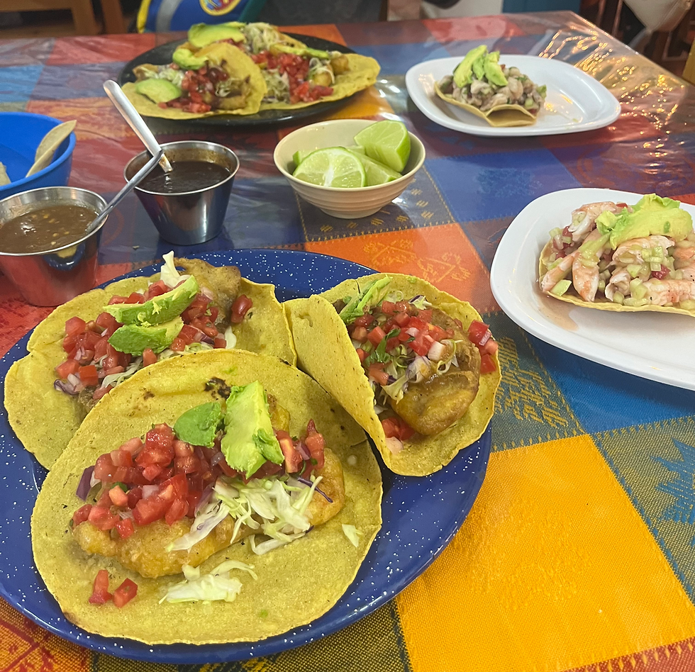 Tacos with avocado and salsa on a blue and white speckled plate, surrounded by lime wedges and sauces on a colorful tablecloth.
