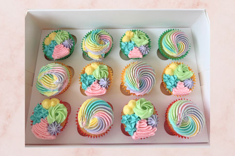 Twelve colorful cupcakes with rainbow frosting in a white box