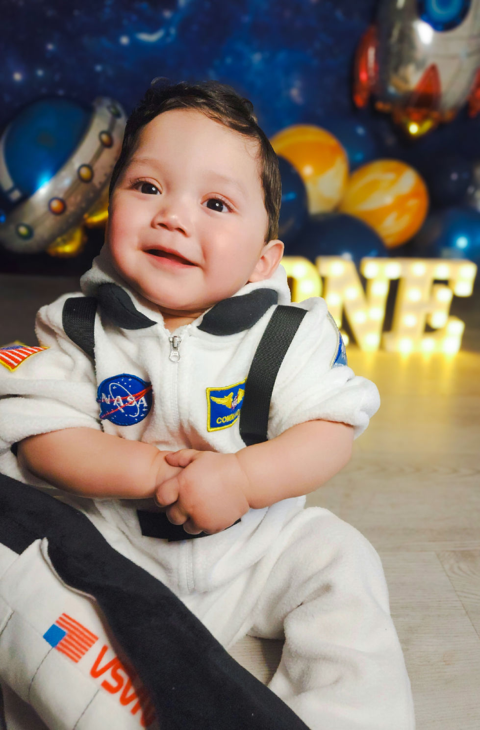 Smiling baby in astronaut costume with balloon background.