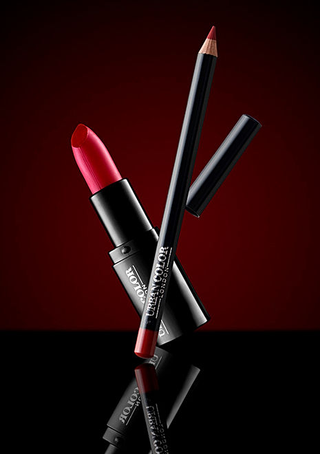 Product photographer image of red lipstick and lip liner with dramatic lighting on a reflective black surface and bold red background for cosmetic product photography.