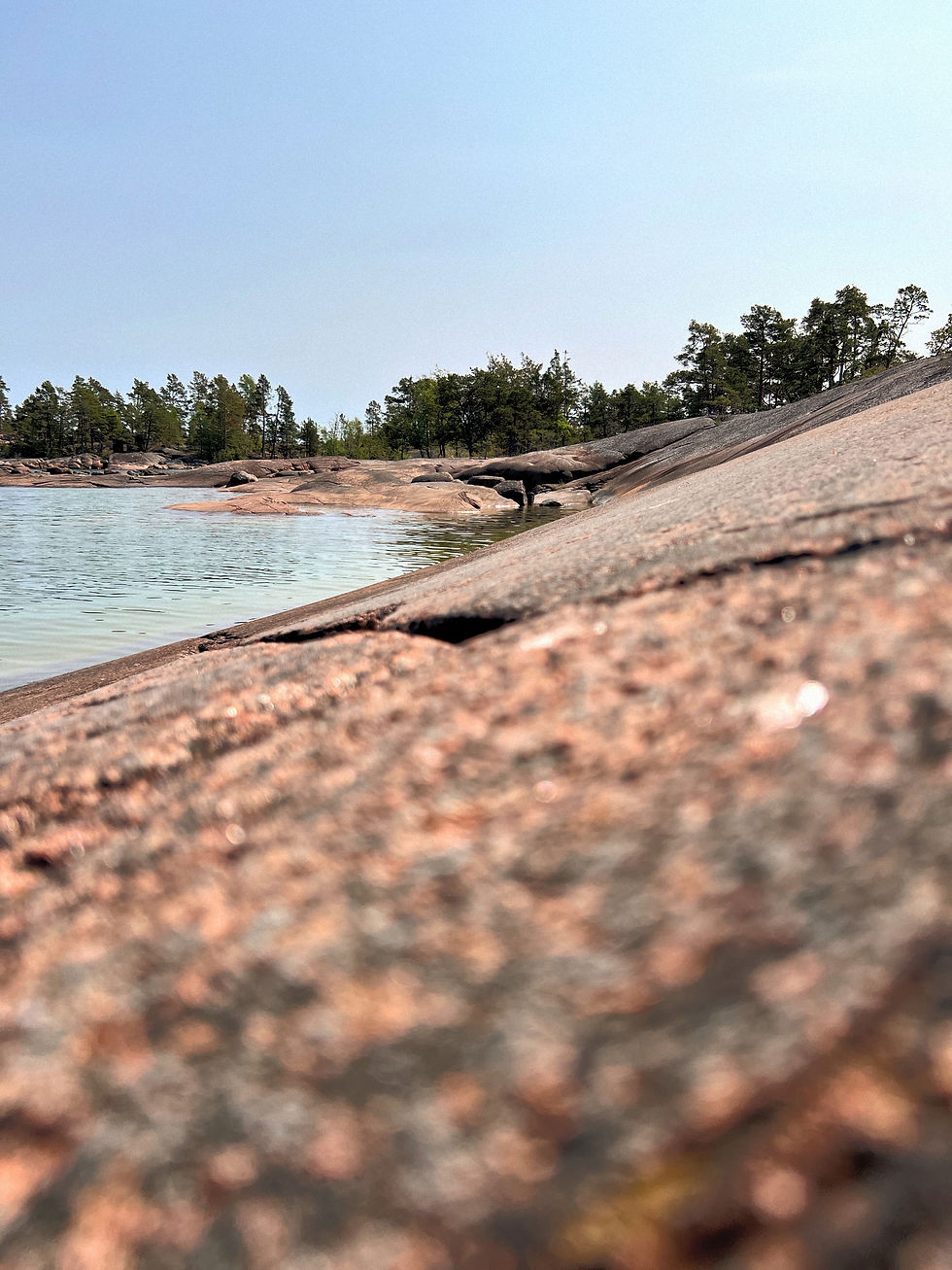 Klippor av röd granit i förgrunden, vatten som glittrar
