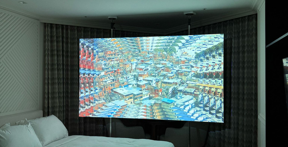 A video is projected onto a screen in a dimly lit hotel room, creating an intimate and contemplative viewing space