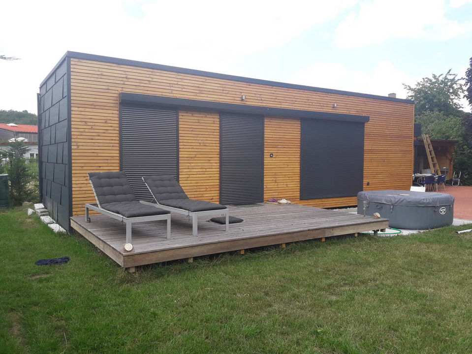 ein modulhaus mit holzfassade und terrasse mit zwei liegestühlen