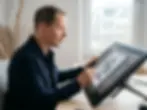 Matthias Thonhofer sitzt an einem Schreibtisch und zeichnet auf einem Wacom Cintiq Grafik-Bildschirm