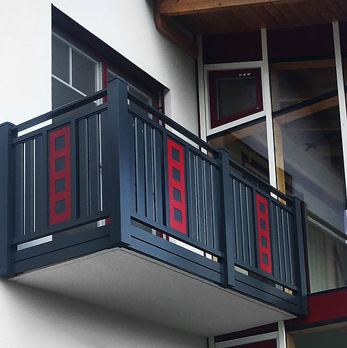 dunkelgraues Balkongeländer mit roten Farbakzenten vor einem Wintergarten