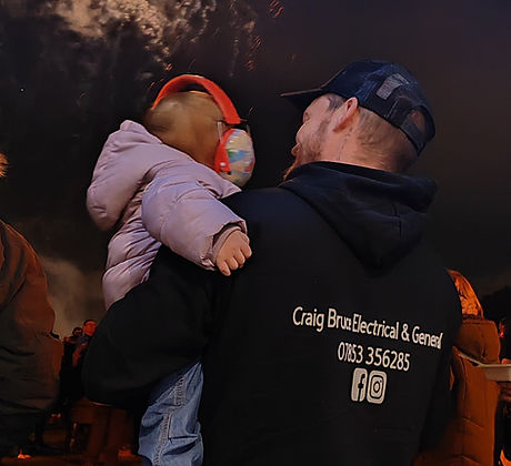 Electrician in branded jumper at fireworks display with child