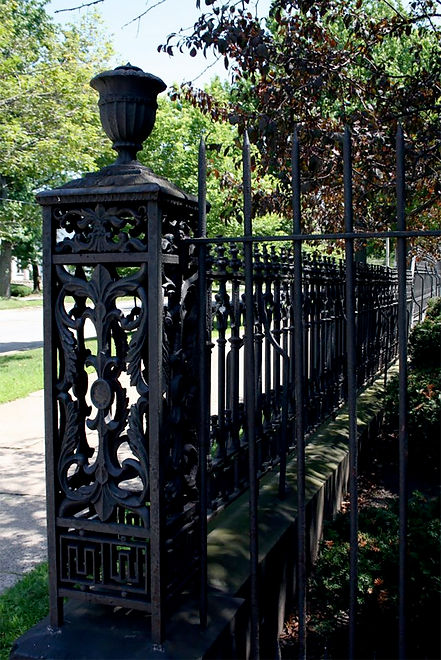 A wrought iron fence in front of a sidewalk