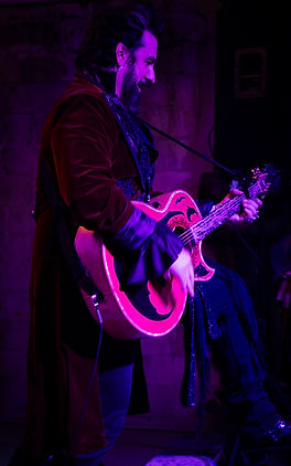 Aurelio Voltaire performing with his leg on the couch of Bearded Social Tavern