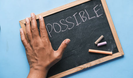 Human hand covering the 'im' in 'impossible' written with chalk on a board