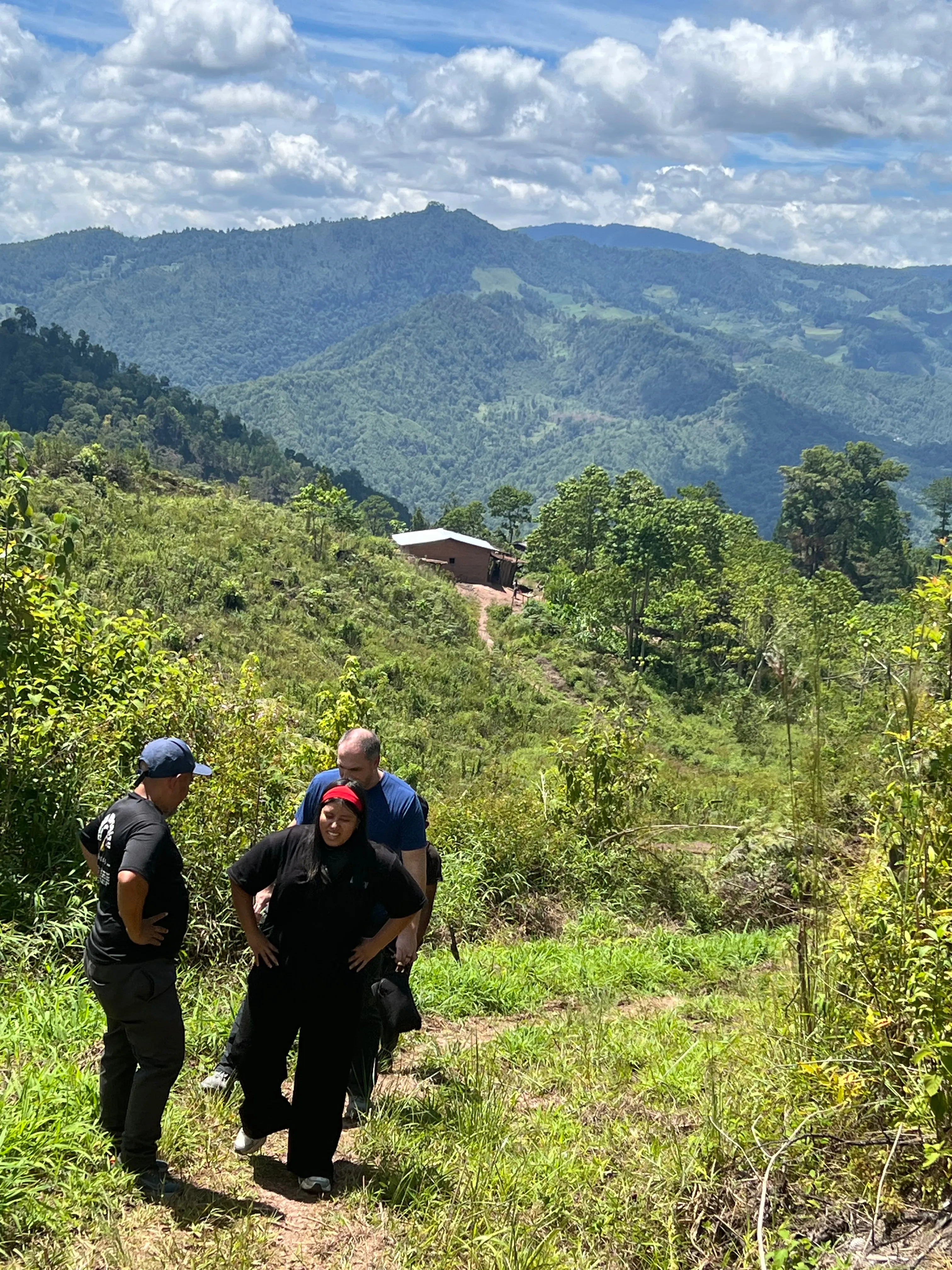 Three adults on a hillside path overlooking forested mountains.