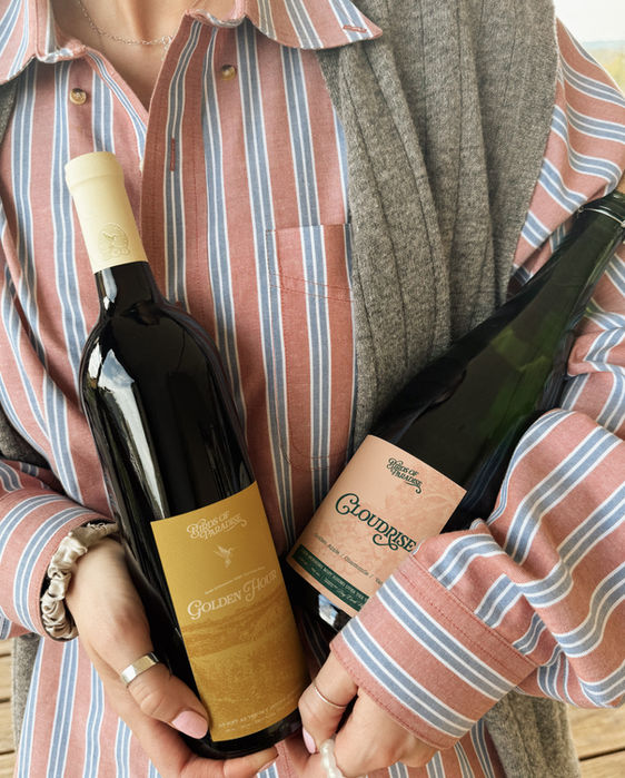 Woman holding two bottles of wine, with labels visible, indoors, close up