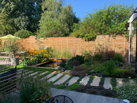 Stepping stone path leading through densely planted garden border with flowering shrubs.