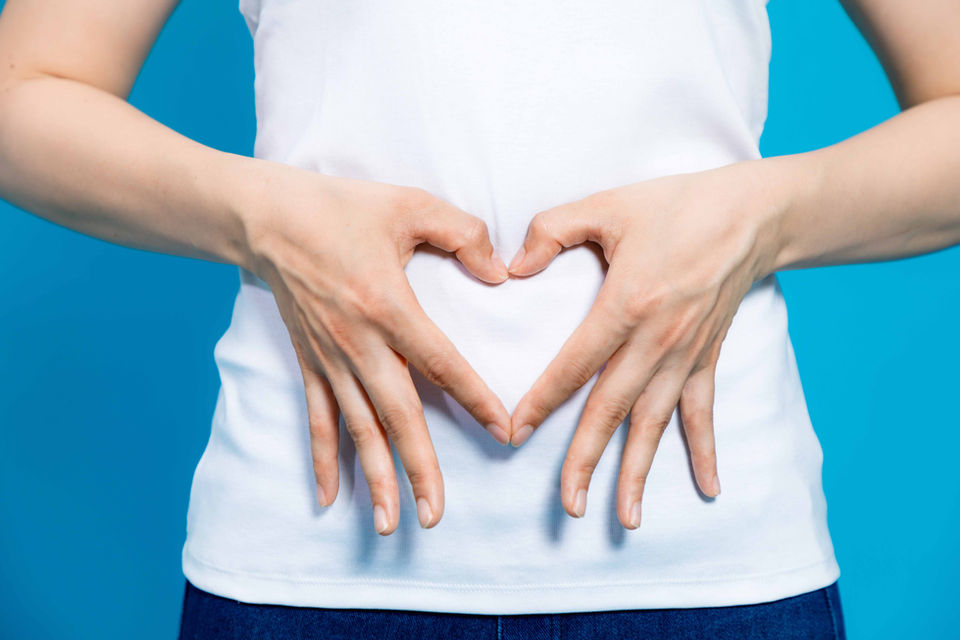 A lady in a white top make a heart symbol with her fingers over her belly.